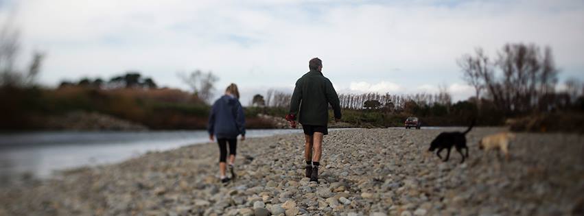 Father and daughter walking dog beside river